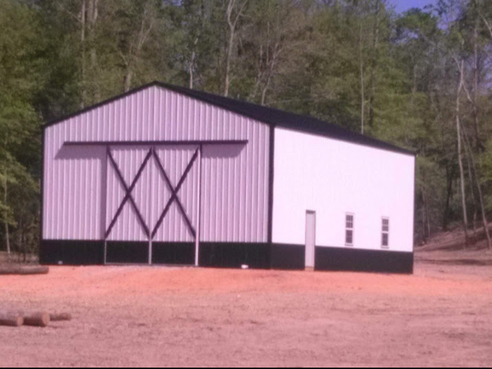 A white and black barn with a sliding barn door in a dirt field.