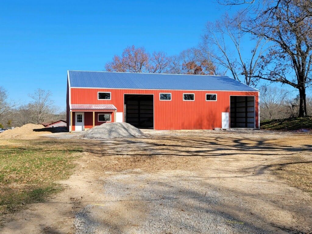 A large red barn is sitting in the middle of a dirt road.