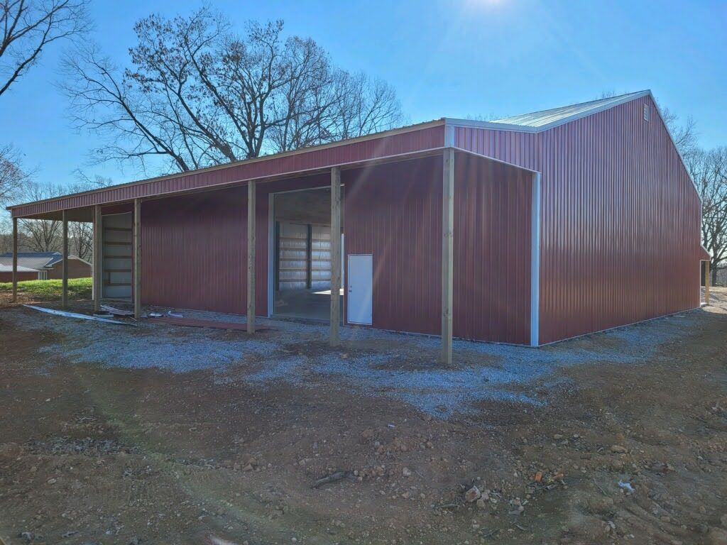 A large red barn with a porch is sitting on top of a dirt field.