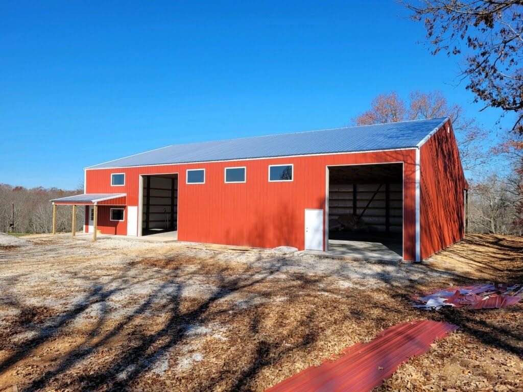 A large red barn is sitting in the middle of a dirt field.