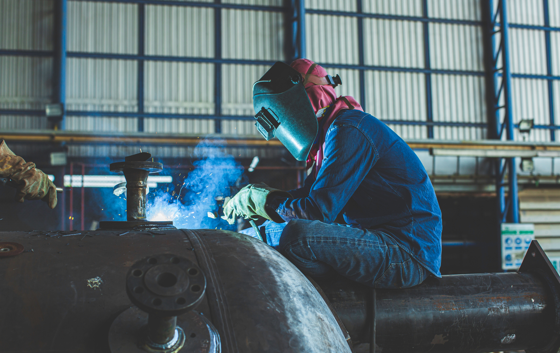 A man is welding a piece of metal in a factory.