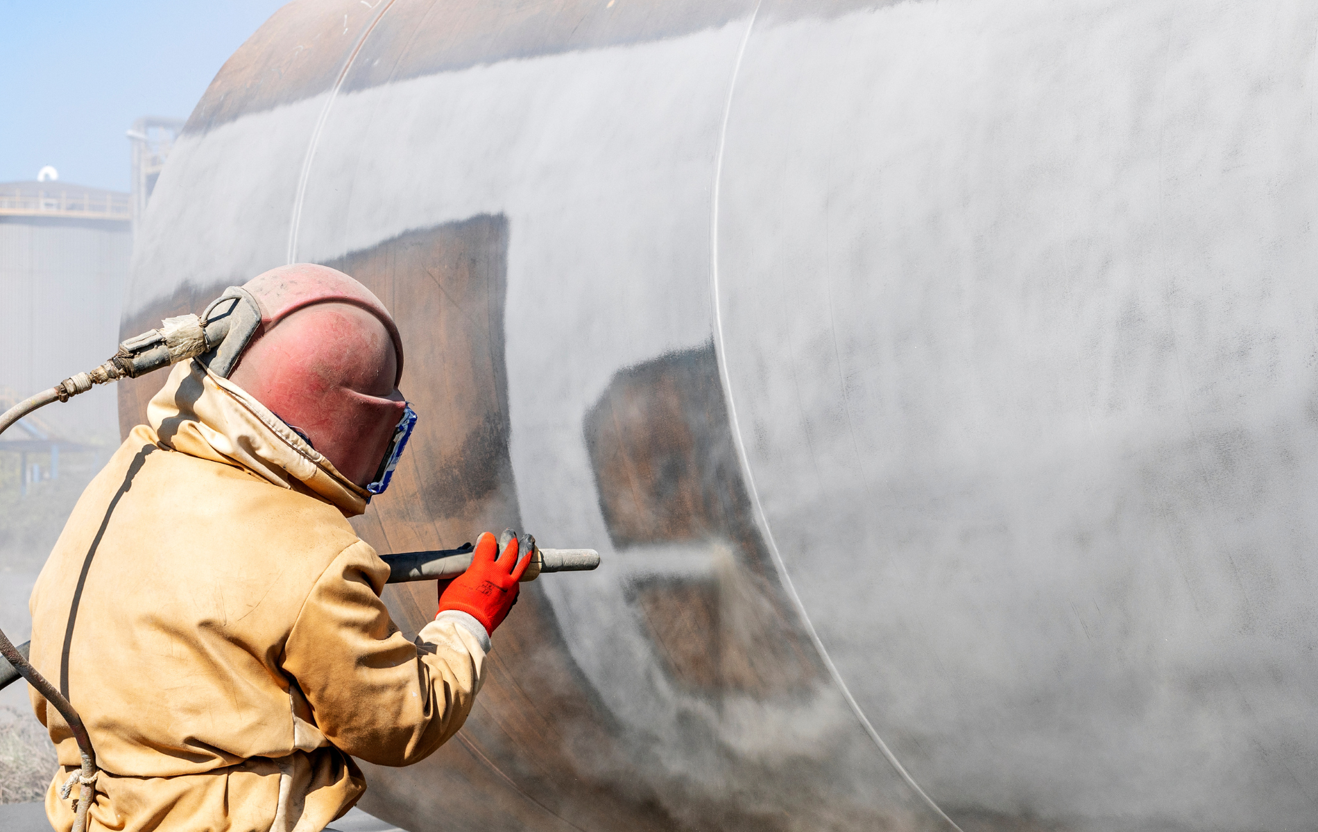 A man wearing a helmet and gloves is sandblasting a wall.