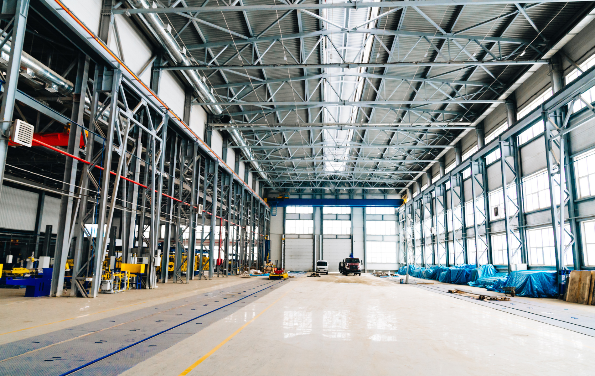 Large industrial warehouse interior with metal beams and a bright floor.