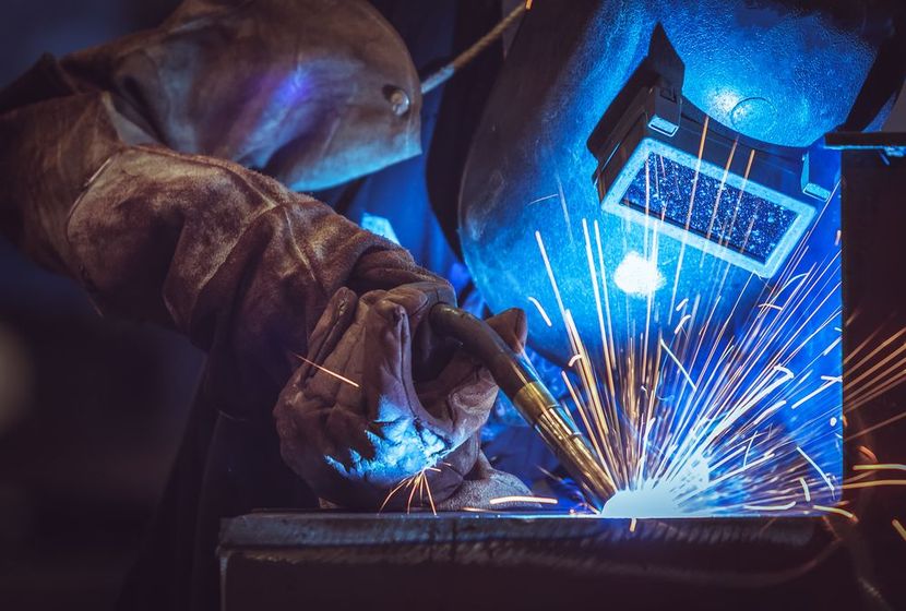 A man wearing a welding helmet is welding a piece of metal.