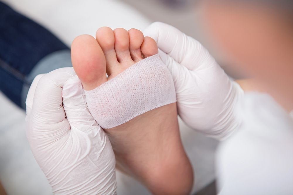 Manos enguantadas vendan el pie descalzo de un niño con una venda blanca.