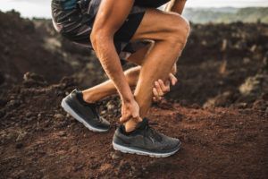 Achilles injury on running outdoors. Man holding Achilles tendon by hands close-up and suffering with pain. Sprain ligament or Achilles tendonitis.