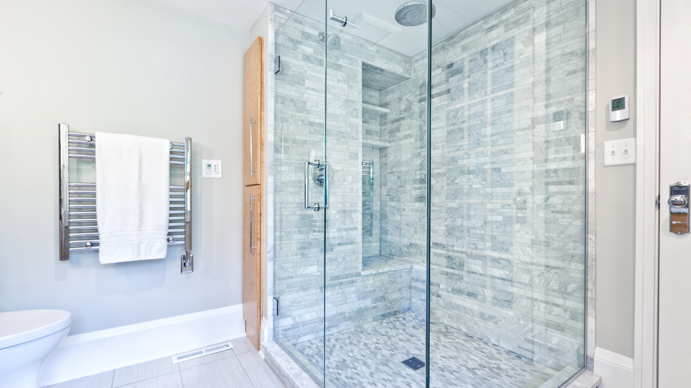A modern bathroom featuring a glass-enclosed shower with gray tiled walls and a white towel hanging on a heated rack.