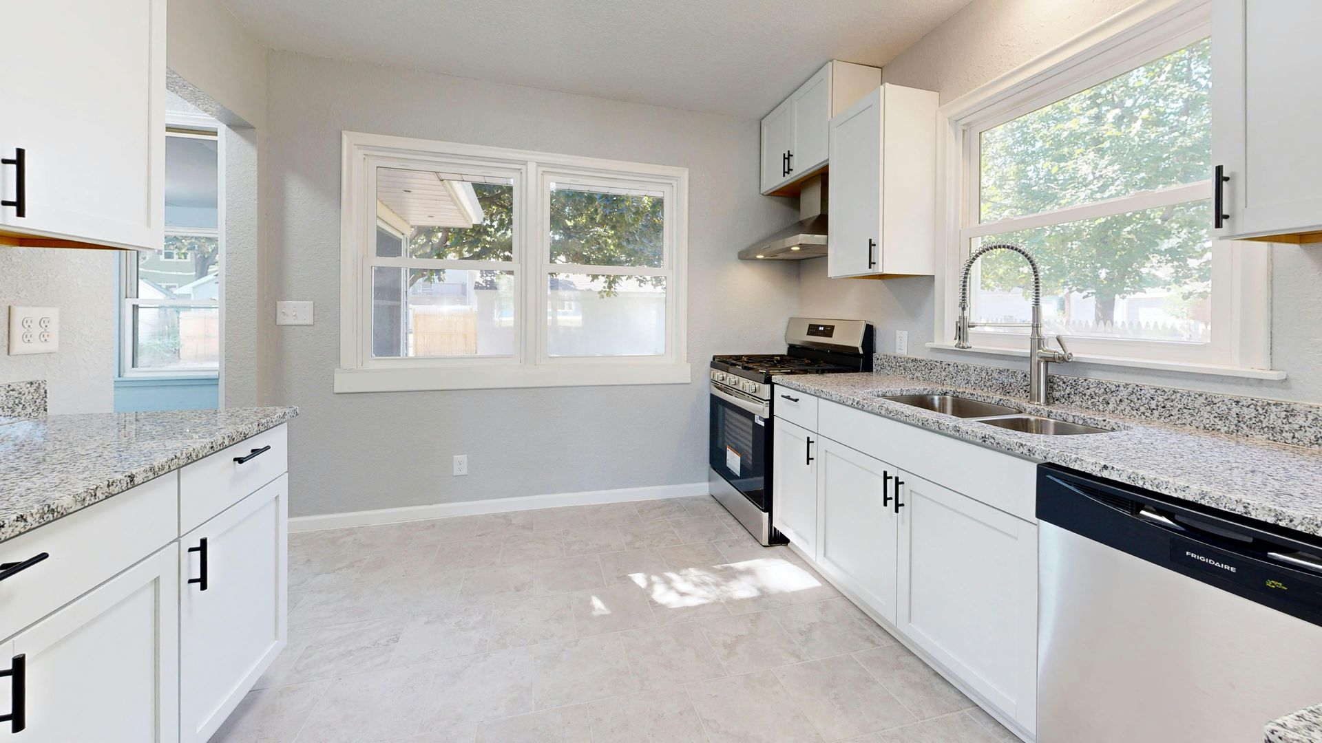 A bright kitchen with white cabinets, speckled granite countertops, stainless steel appliances, and large windows.