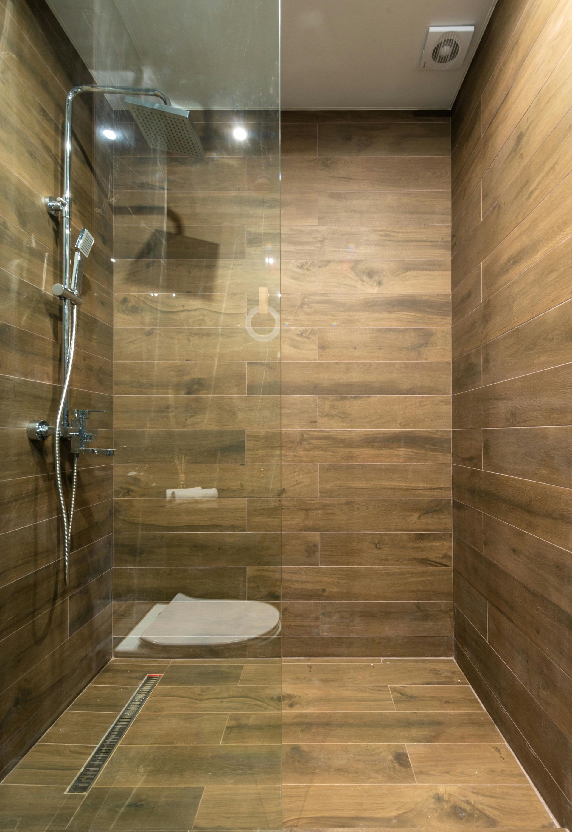 A modern walk-in shower with wood-patterned tile walls and floor, a glass partition, and a chrome shower fixture.