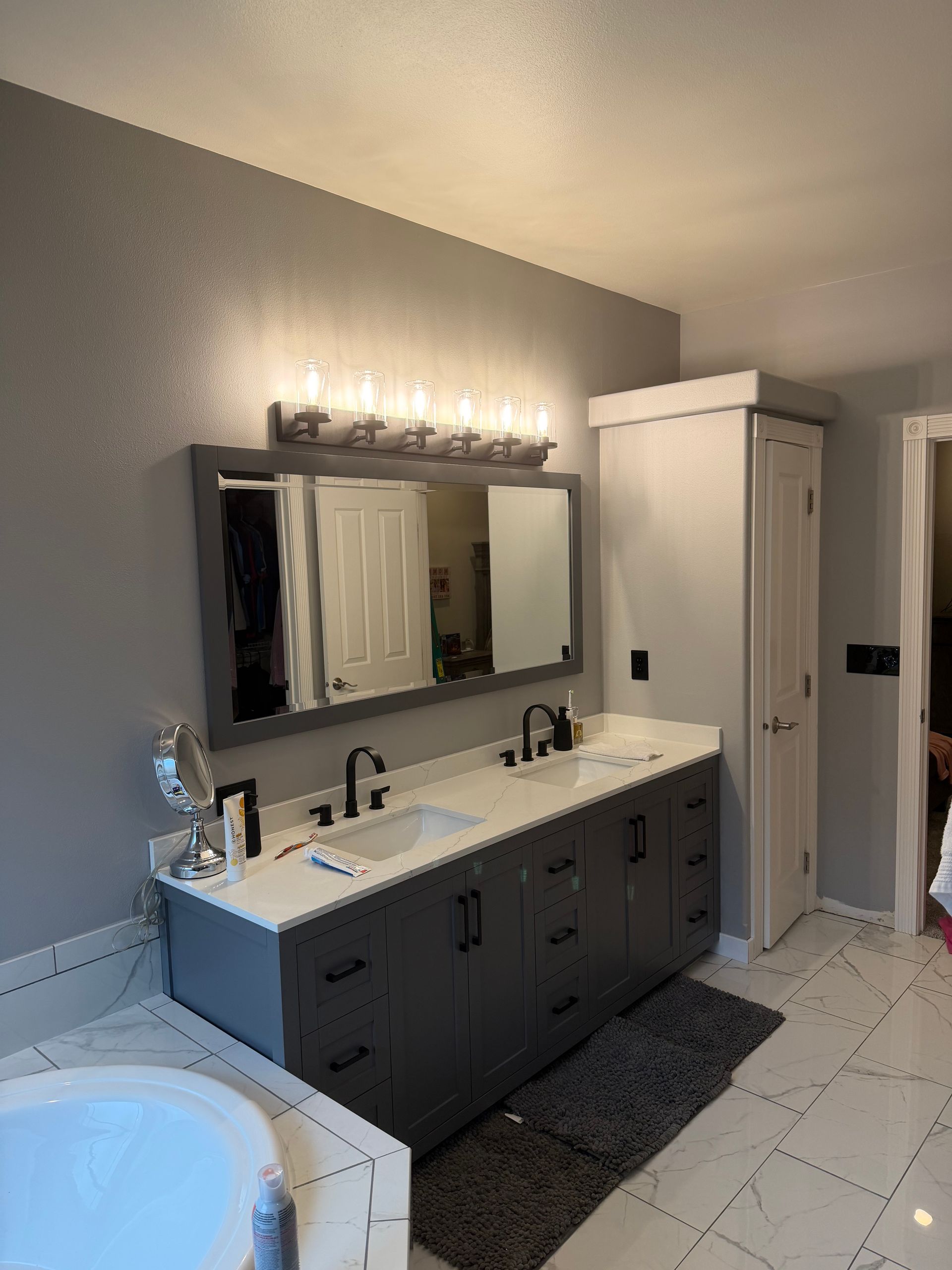 Bathroom with gray cabinets, white countertop, large mirror, and overhead lights.