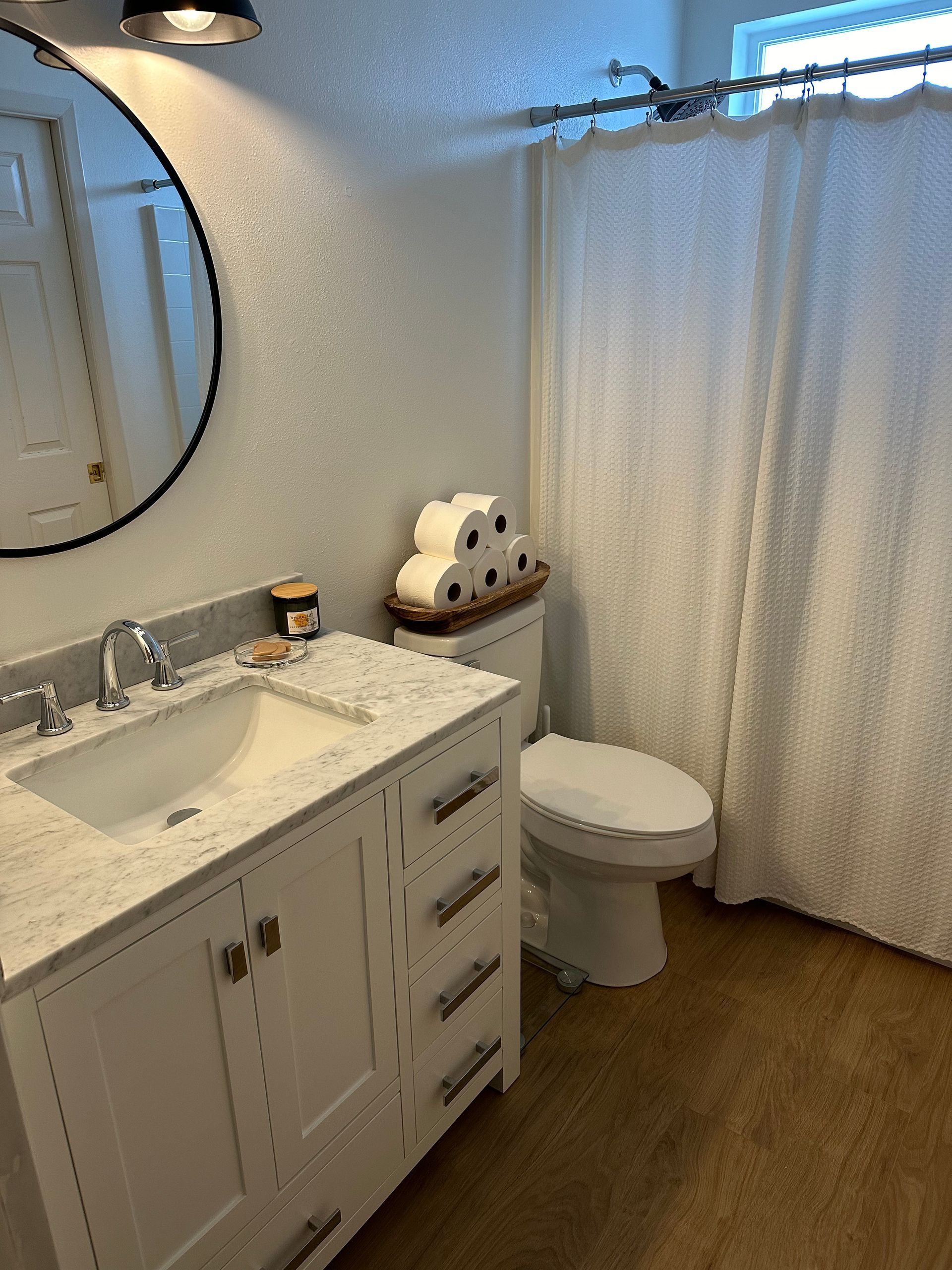 Bathroom with white vanity, round mirror, toilet with stacked toilet paper, and white shower curtain.