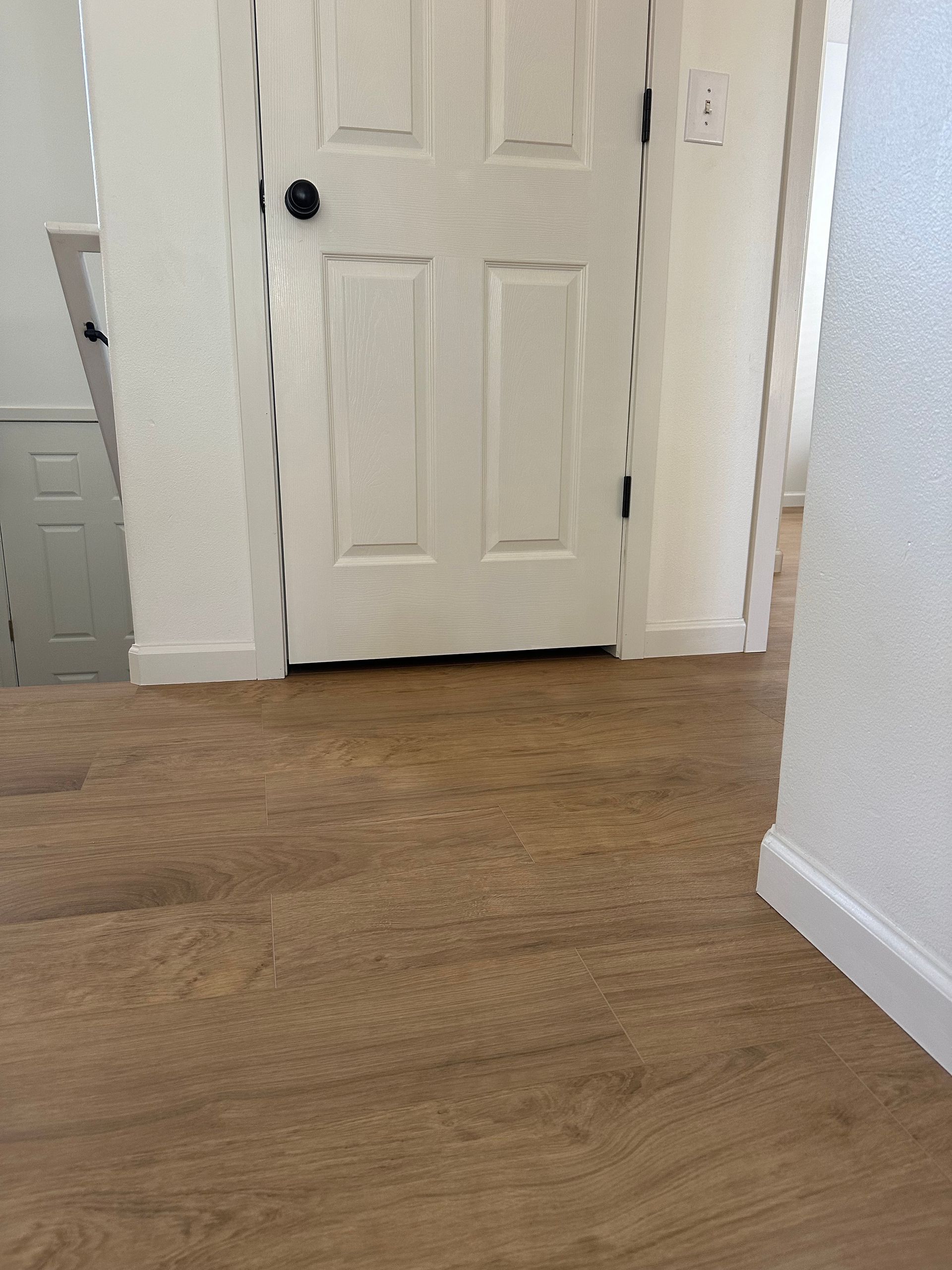 Wooden floor leads to a white door with a black handle in a hallway with white walls.
