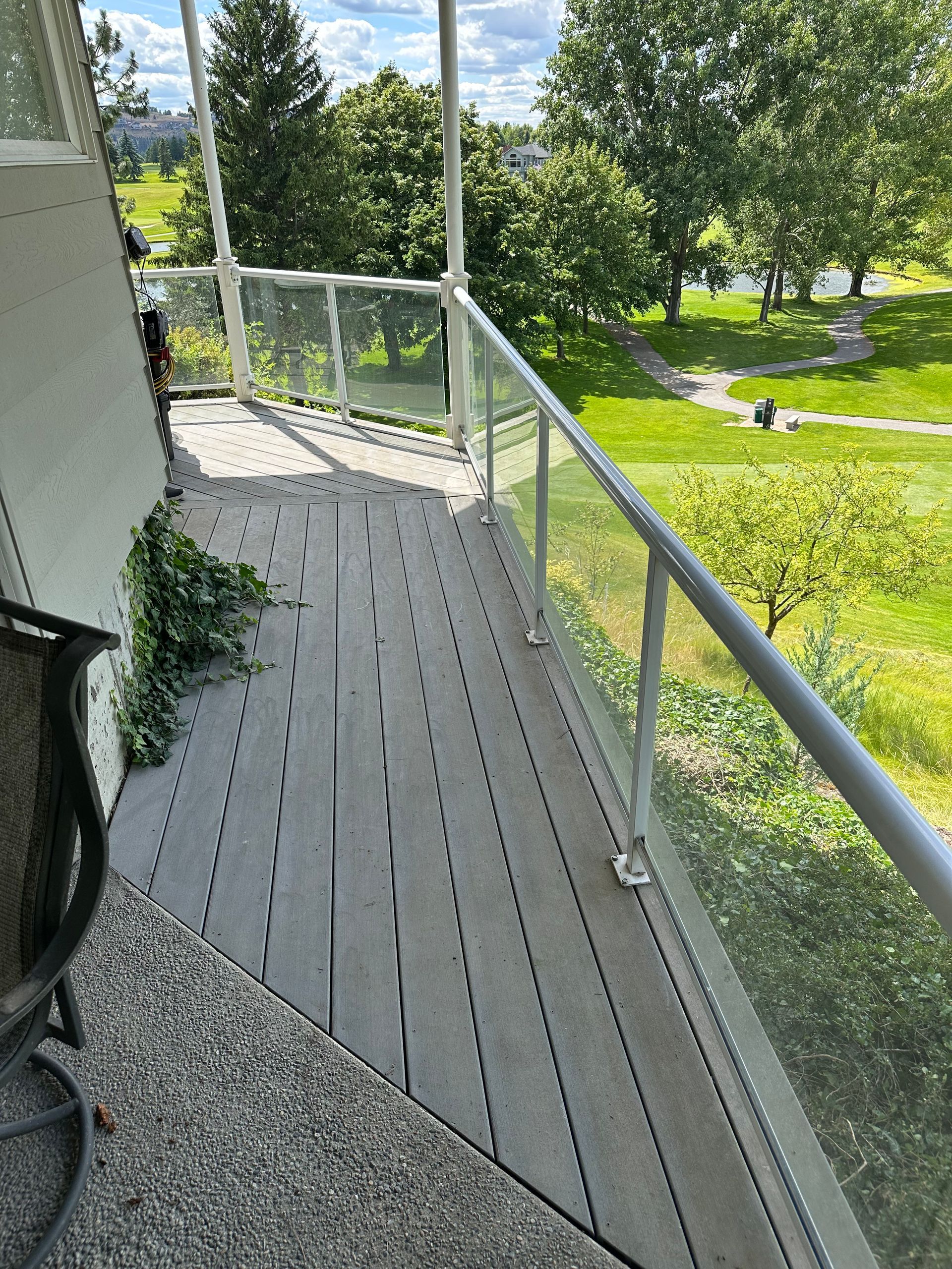 Deck with glass railing overlooking a green golf course and trees.