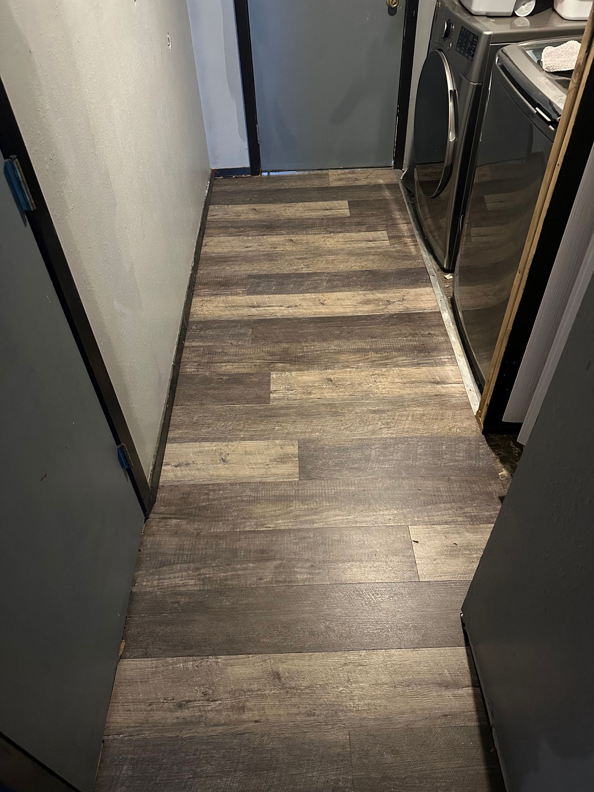 Narrow hallway with wood-look flooring, appliances on the right, and doors on both sides.