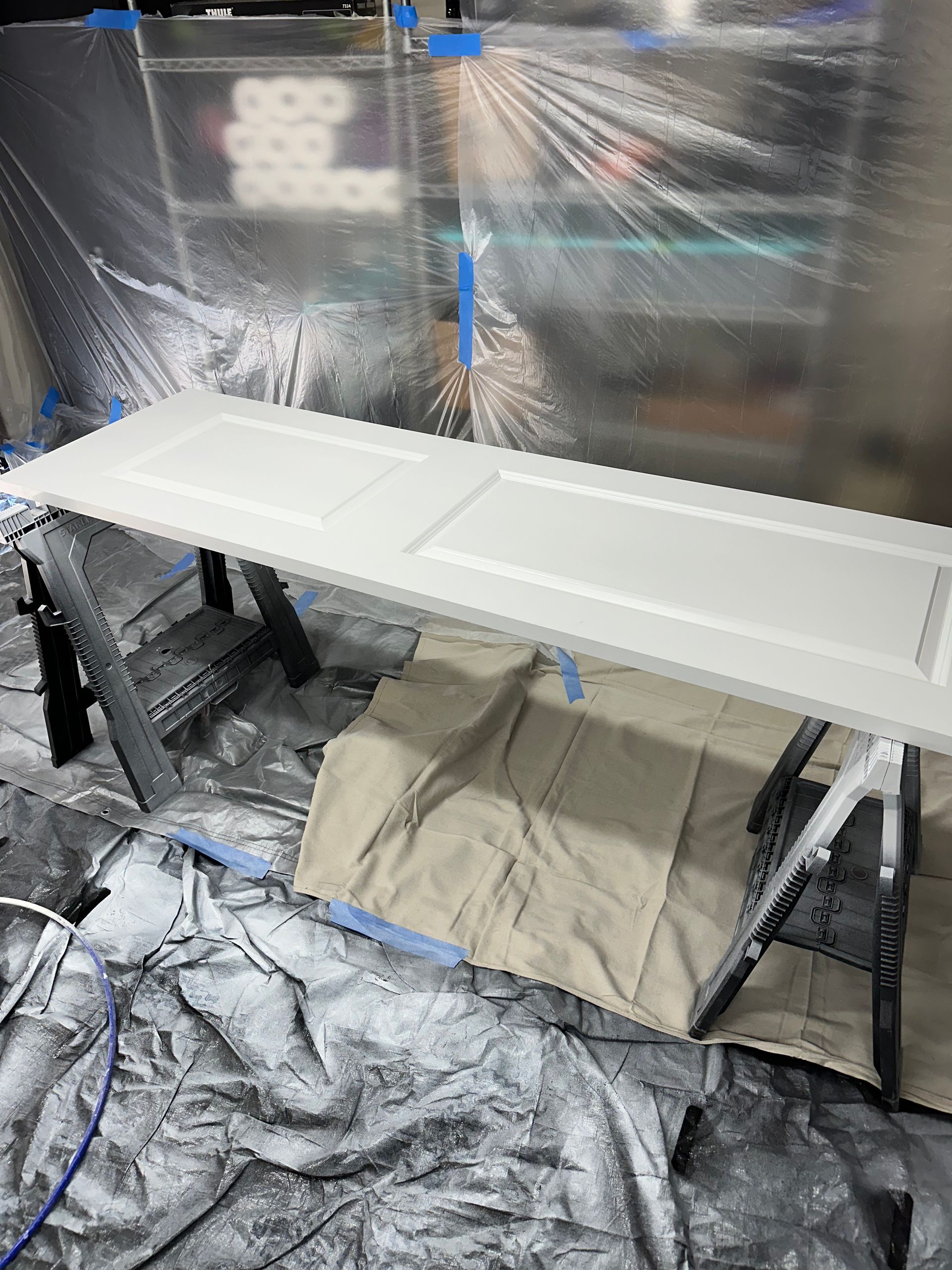 A white door laid on sawhorses in a protective spray-painted workspace.