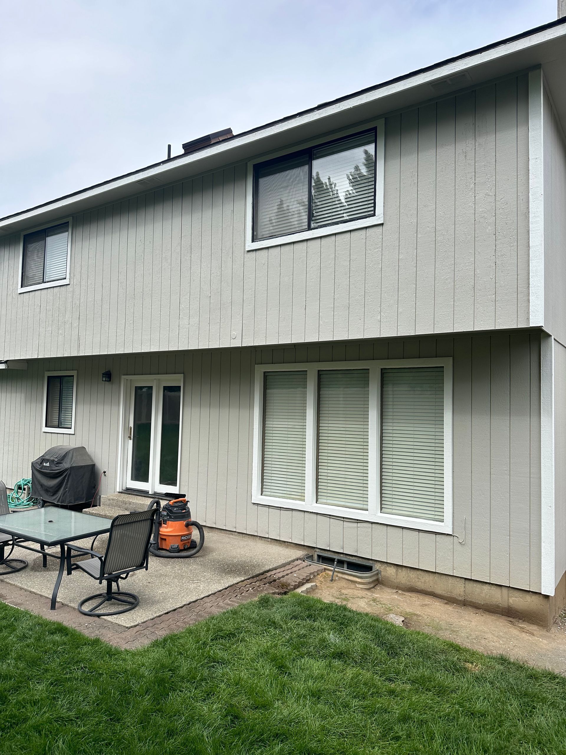 Back of a two-story house with gray siding, white trim, patio, and green lawn.