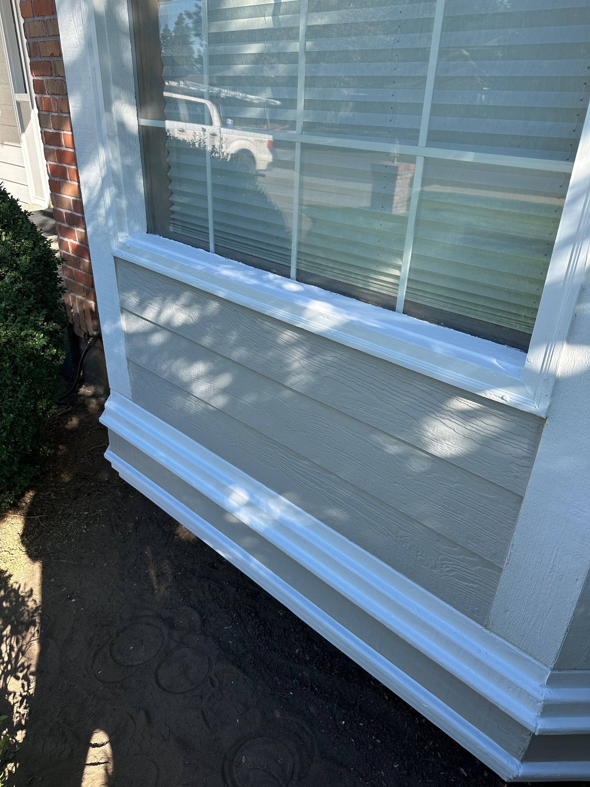 Exterior corner of a building with a window and gray siding with white trim.