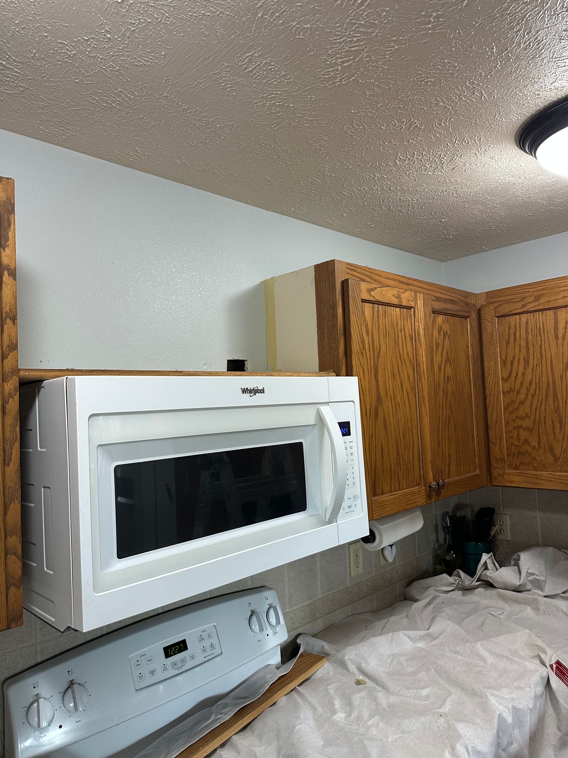 White microwave over a stove beneath wooden cabinets in a kitchen.