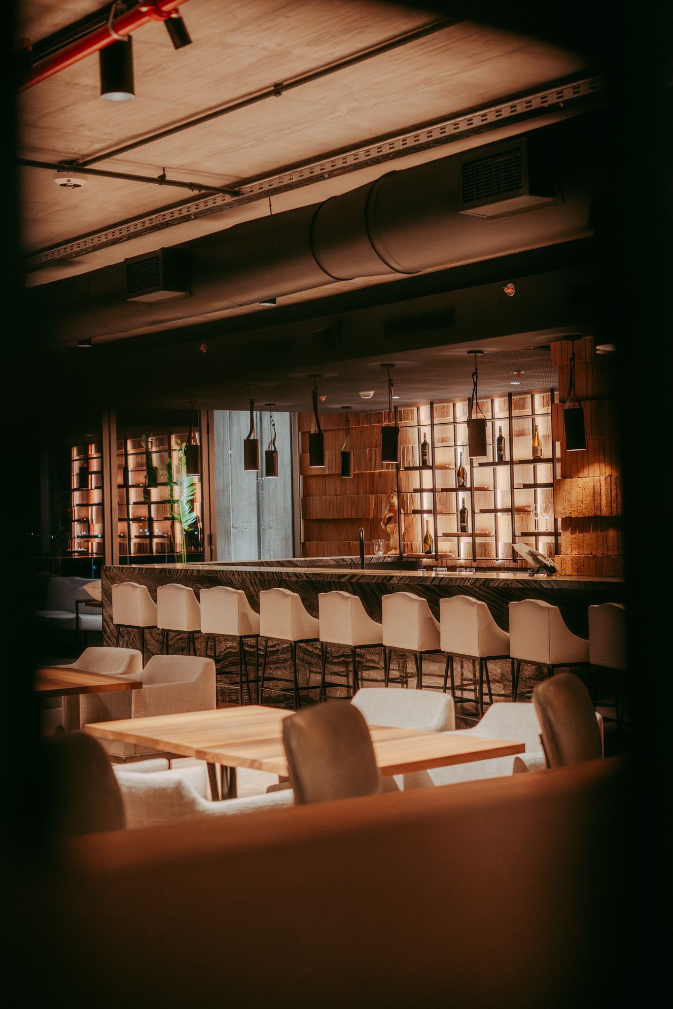 Interior de un restaurante o bar, con barra iluminada y mesas con sillas. Iluminación cálida en todo el local.