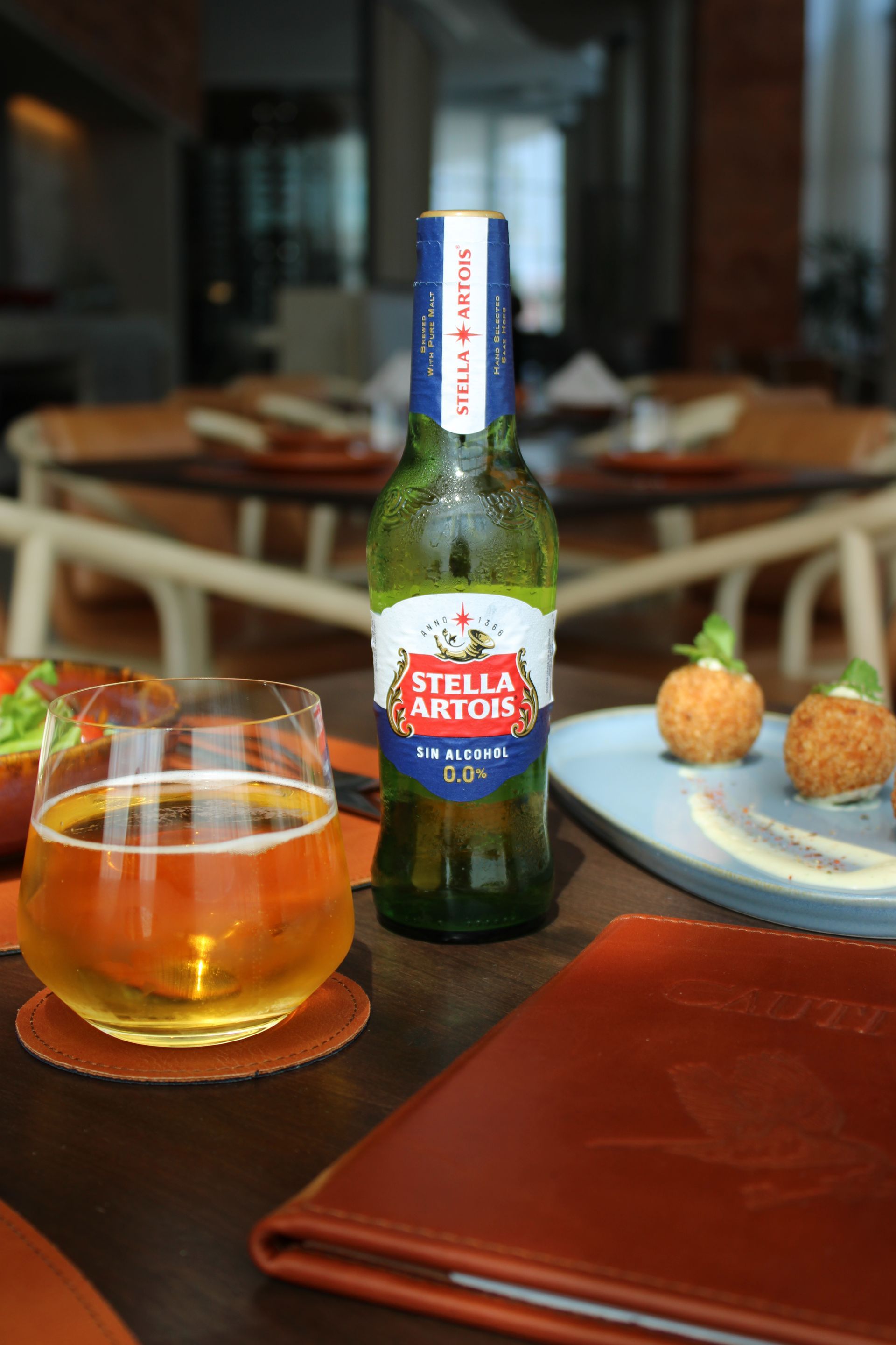 Botella y vaso de cerveza Stella Artois sobre una mesa con comida, entorno de restaurante.