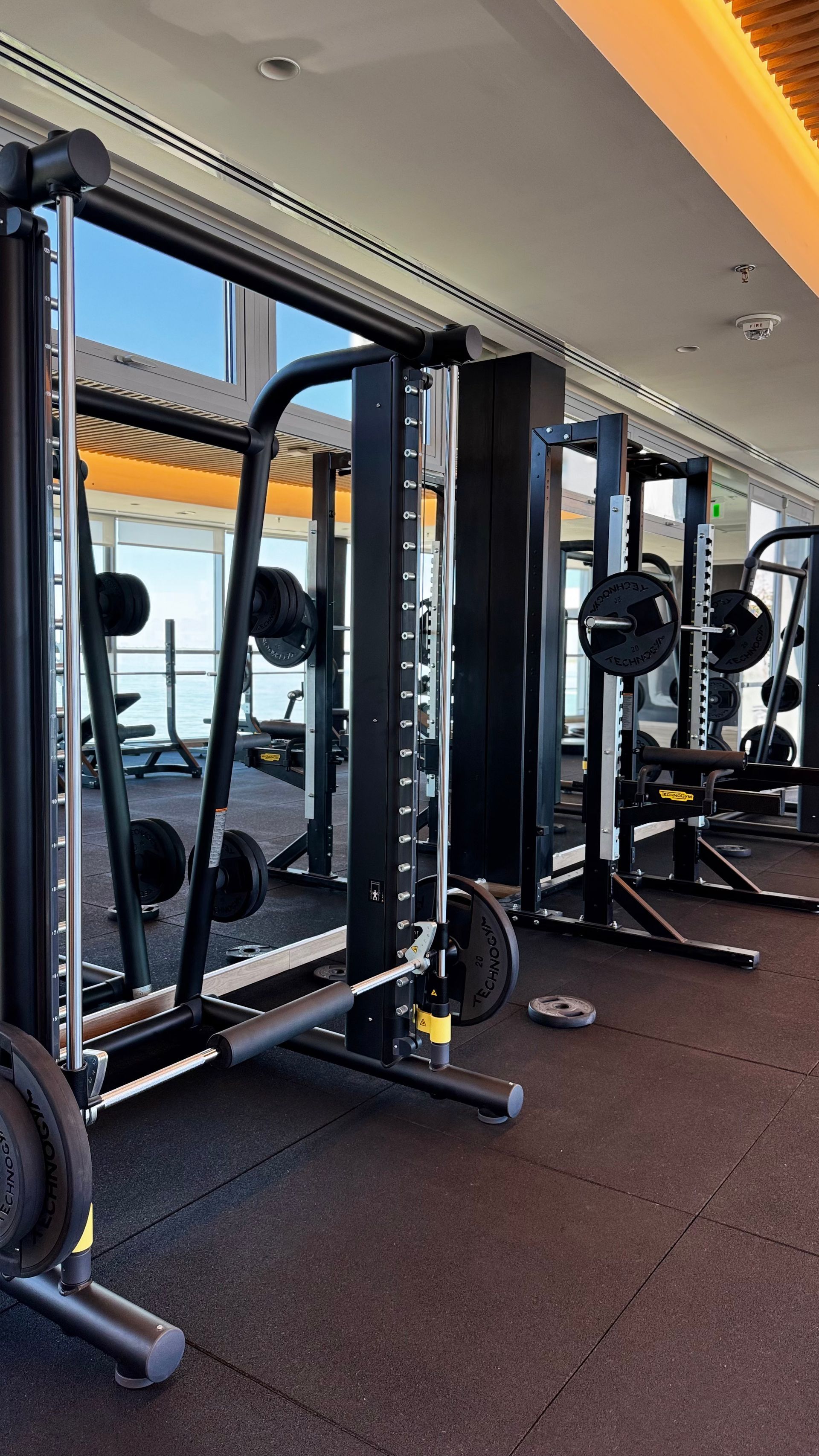 Interior de gimnasio con máquinas de pesas, barras y pesas sobre suelo negro.