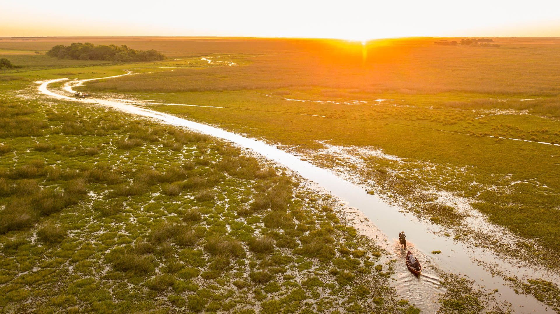 Un río estrecho serpentea a través de una pradera pantanosa hacia una brillante puesta de sol.