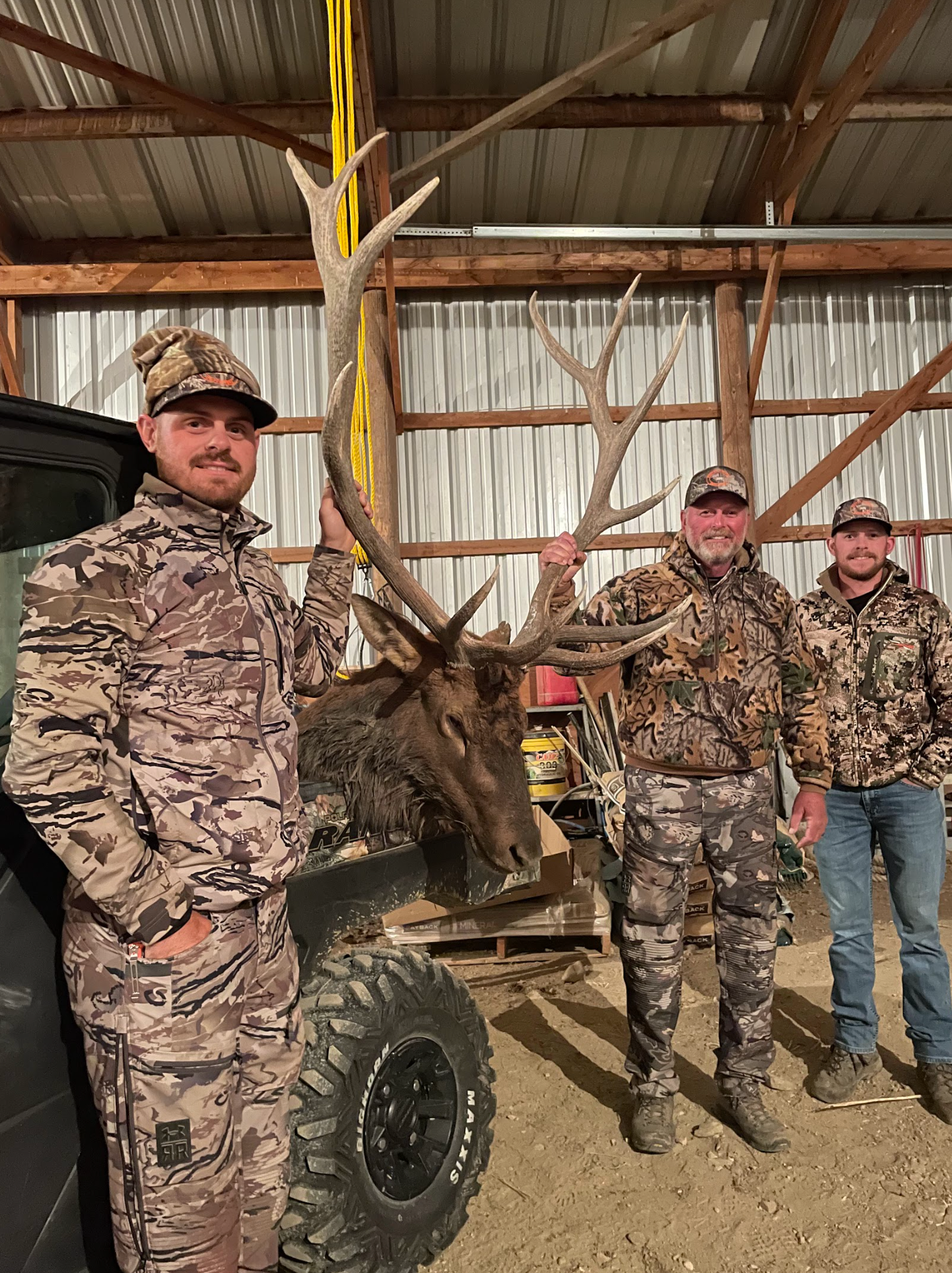 Three men are standing next to a large deer in a barn.