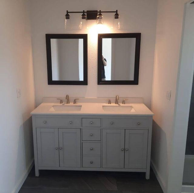 Bathroom with a gray vanity, two mirrors, and overhead lighting.