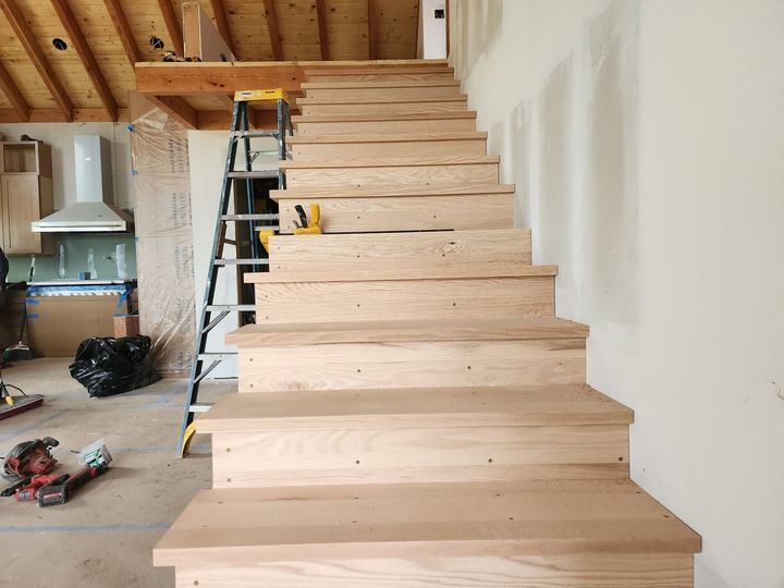 Wooden staircase under construction with visible treads, ladder, and tools.