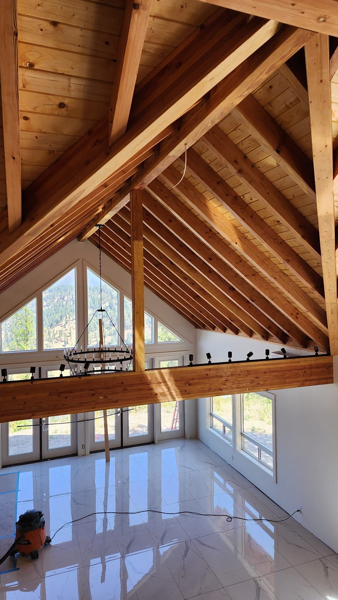 Interior of a house under construction. Vaulted ceiling with wooden beams, large windows, and a shiny floor.