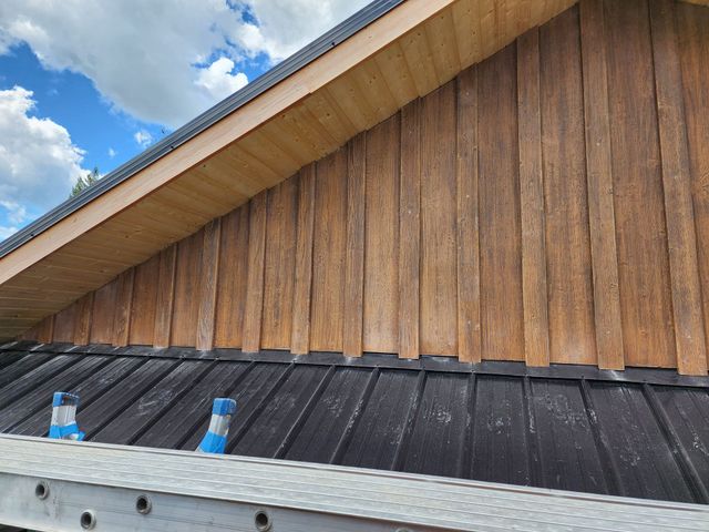 Wooden siding on a building with a black metal roof, seen against a blue sky.