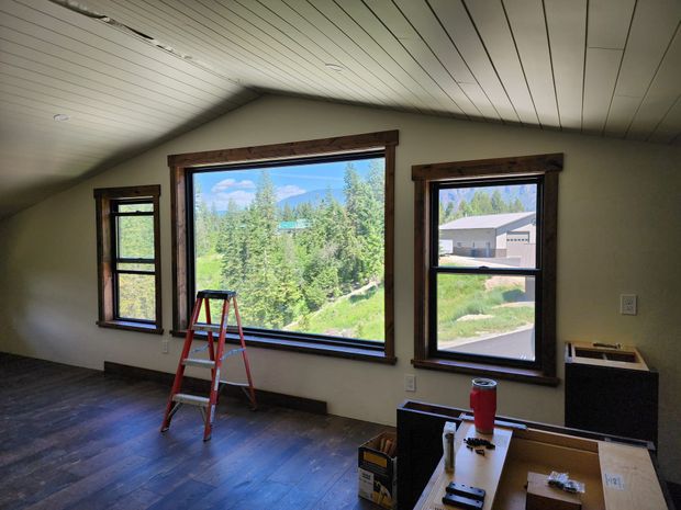 Interior room with three windows, a ladder, and a view of trees and mountains. Dark wood trim.