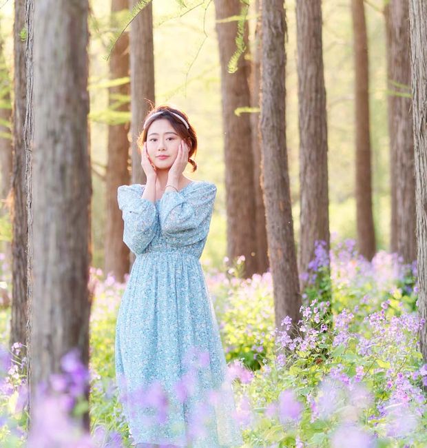 happy woman in woods surrounded by purple wildflowers