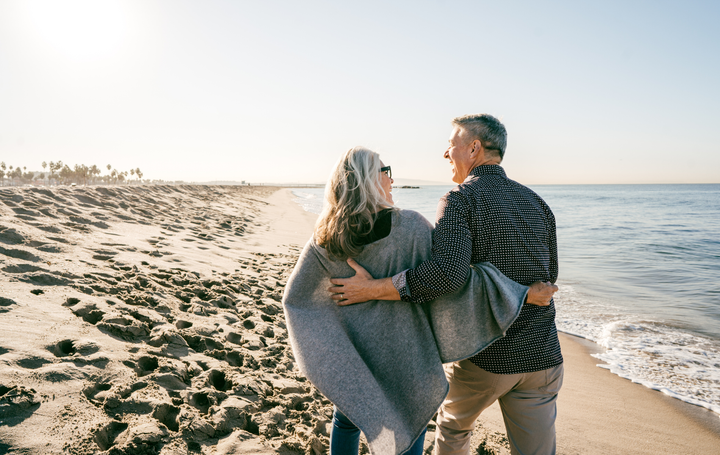 Couple hugging on a sandy beach at sunset, wrapped in a gray blanket near the shoreline