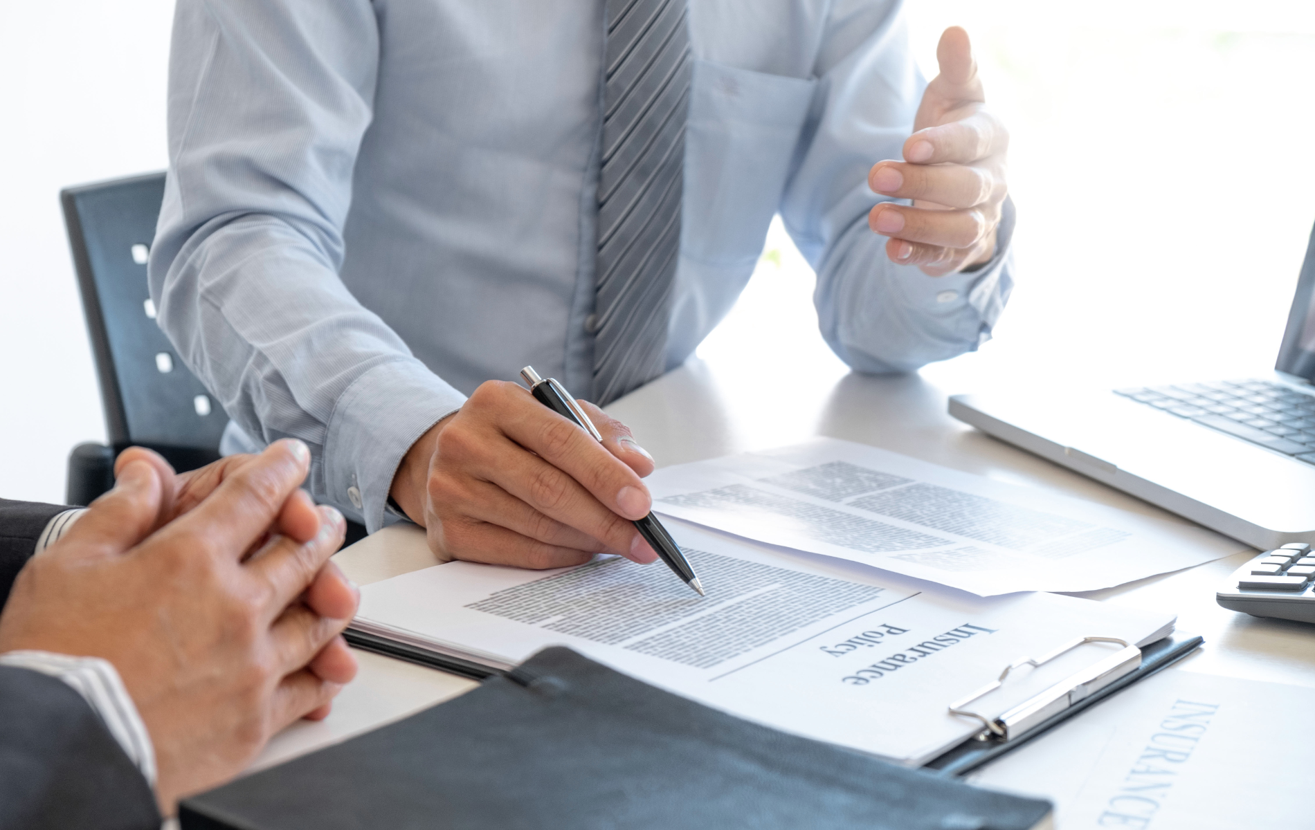 Business meeting with two people discussing documents at a desk with a laptop and clipboard