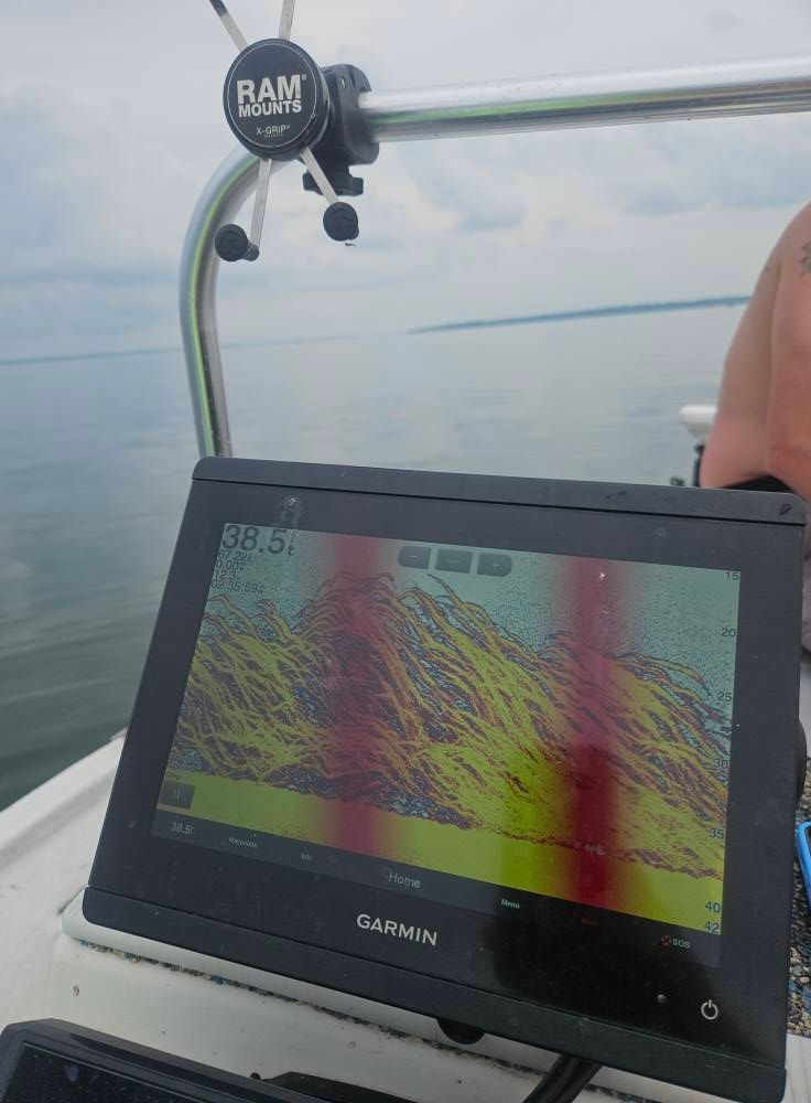 A Garmin marine chartplotter on a boat displays sonar data showing underwater structure against a calm, overcast backdrop.