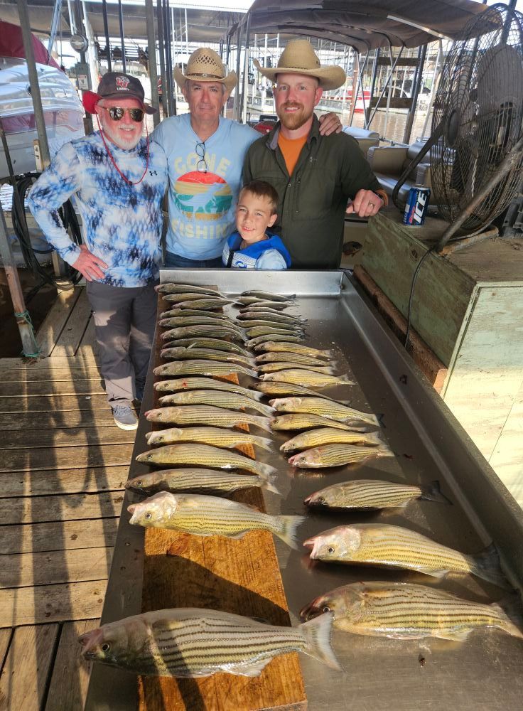 Three people stand behind a large metal table covered with a large catch of striped fish on a wooden dock.
