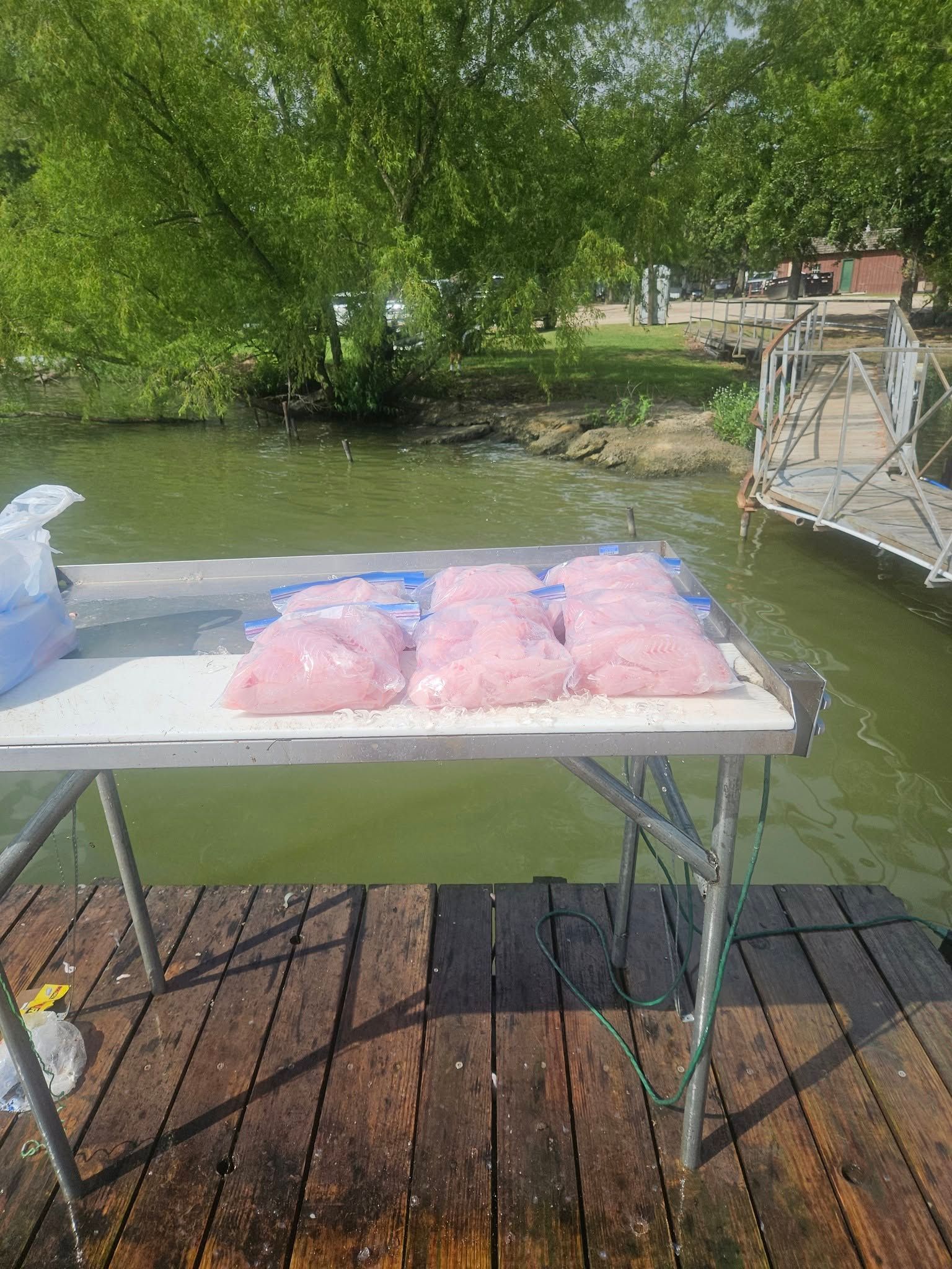 Several bags of pink substance sit on a white table on a wooden dock overlooking a lake.