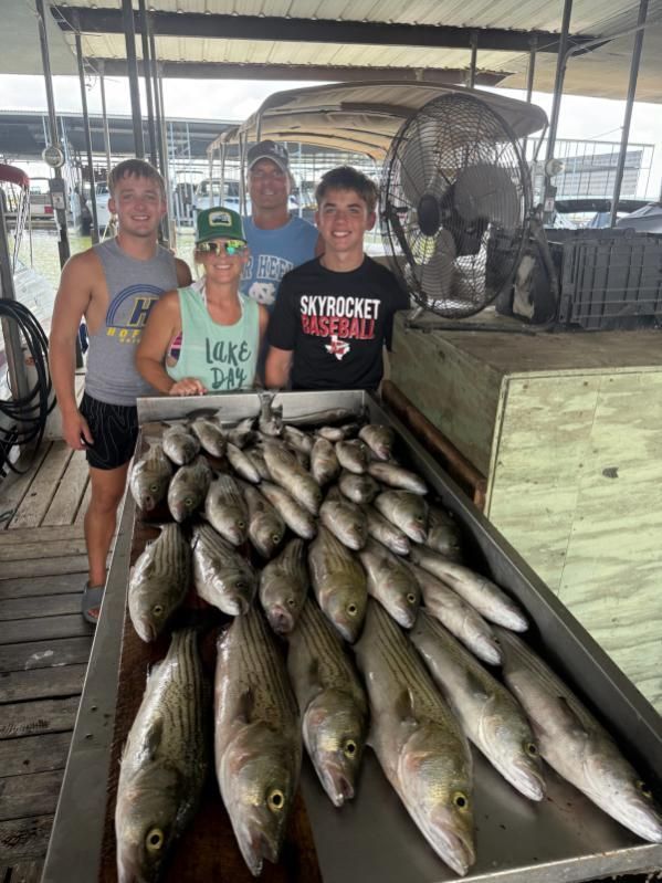 A group of four people stands behind a large metal cleaning table displaying many freshly caught striped bass.