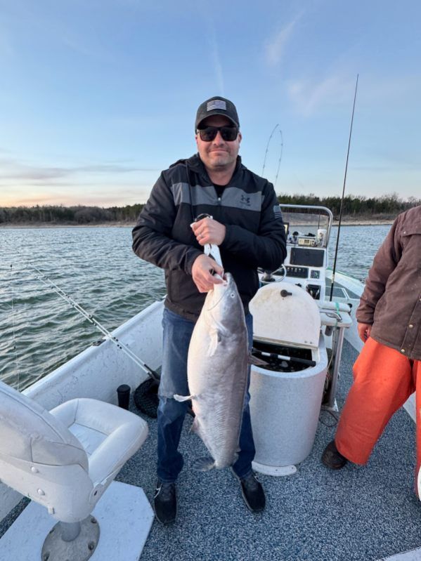 A person holding a large fish on a boat on a lake under a clear blue sky.