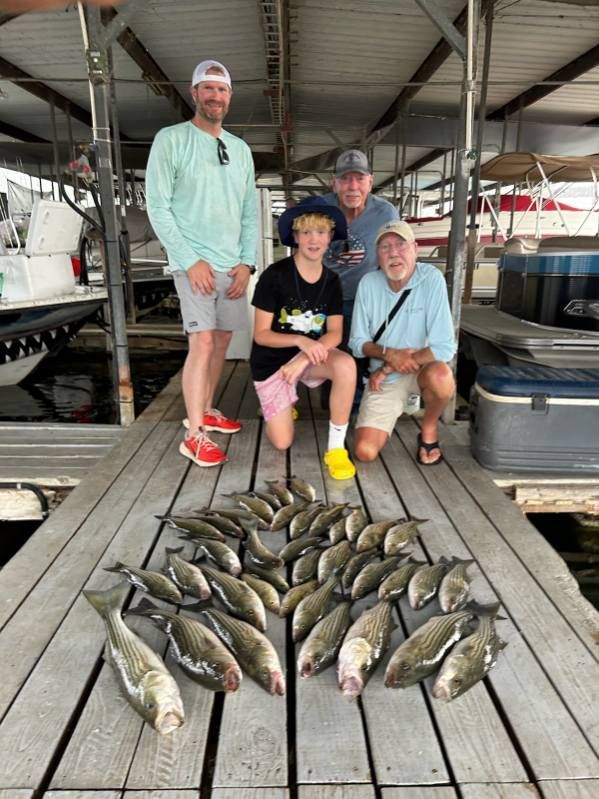 Four people pose on a wooden dock with a large catch of fish spread out on the planks in front of them.