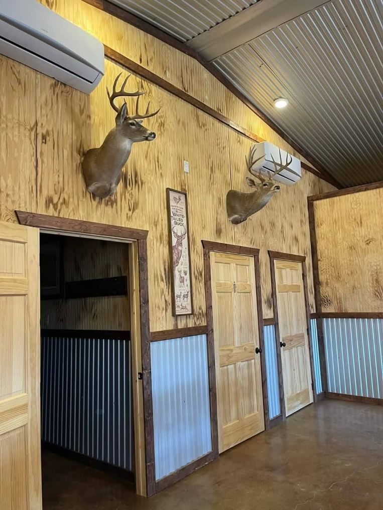 Rustic room with plywood walls, metal wainscoting, and two deer taxidermy mounts above wooden doorways.
