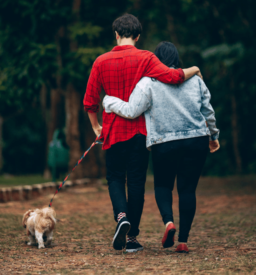 a couple walks their dog while arm in arm