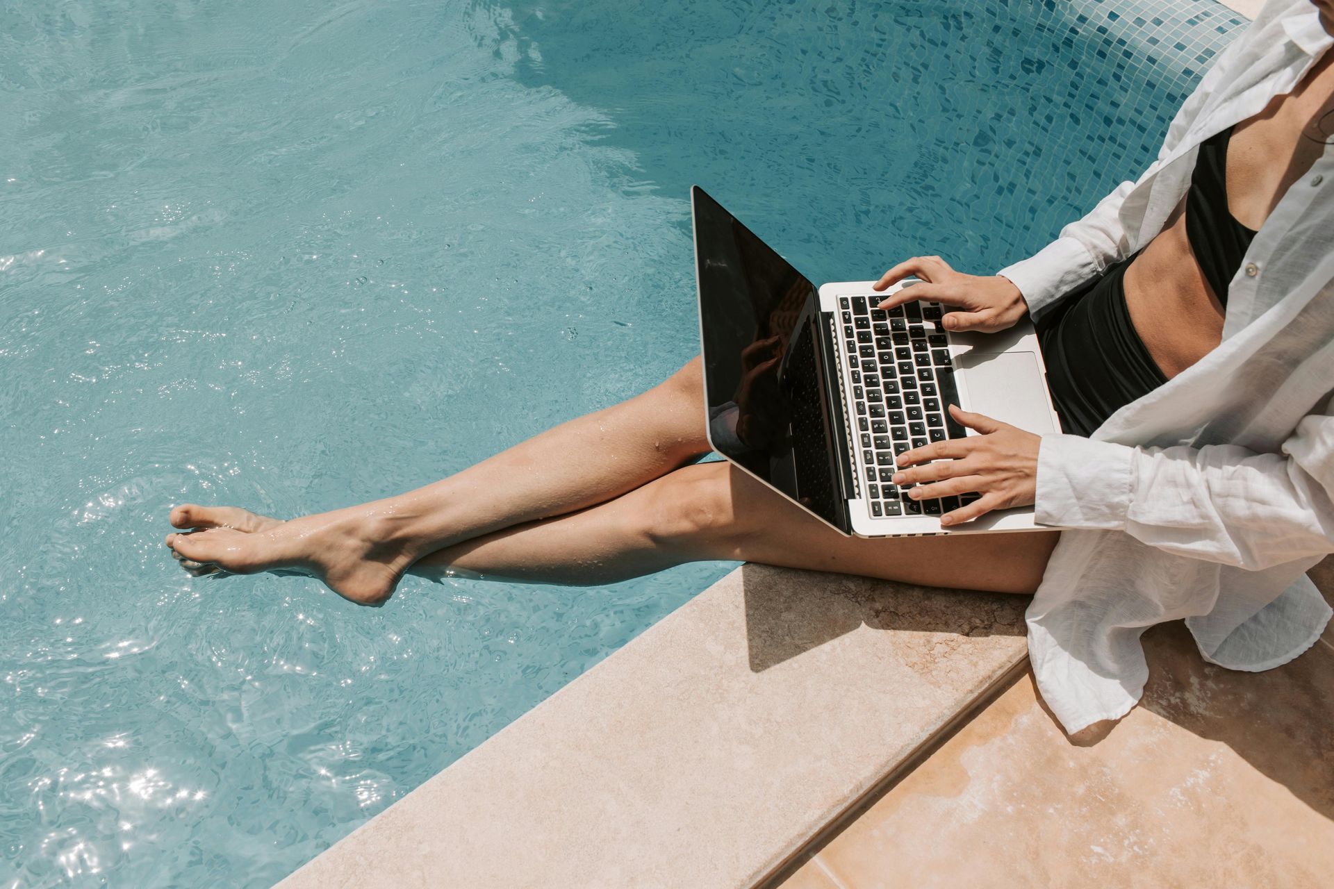 Nomadic remote worker, working on her laptop by the pool.