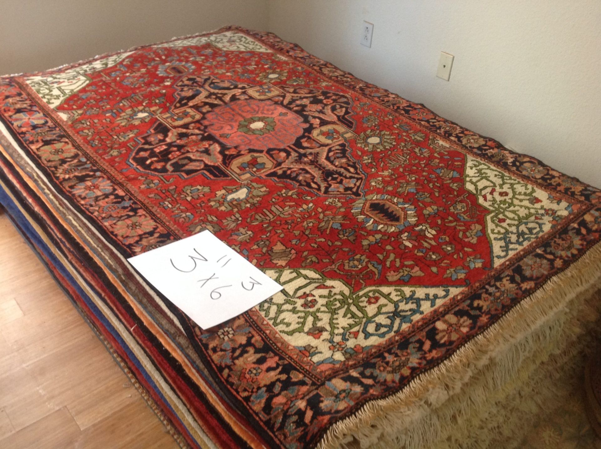 A stack of rugs on a wooden floor with a piece of paper on top that says ' cal ' on it