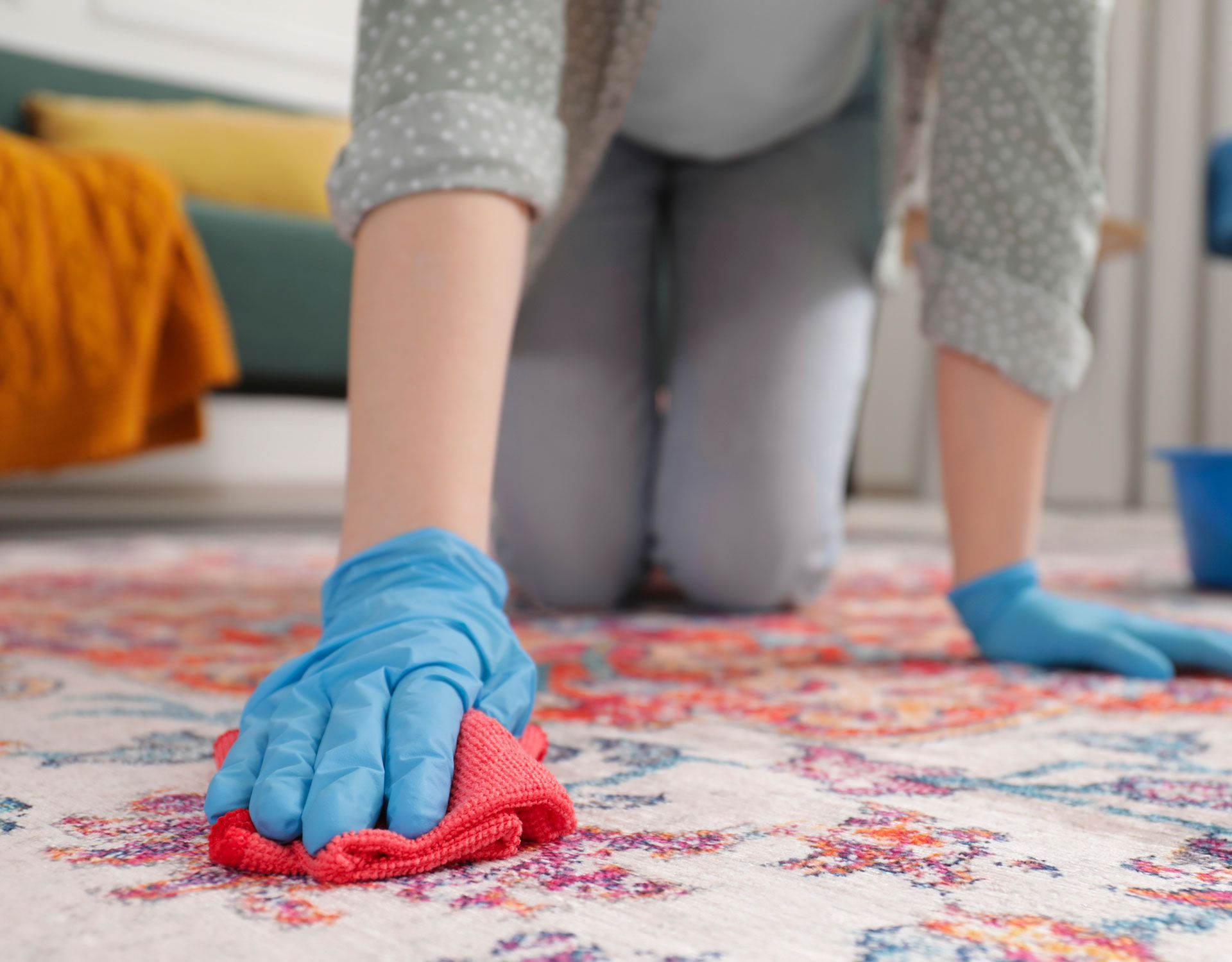 A woman wearing blue gloves is cleaning a rug with a cloth.