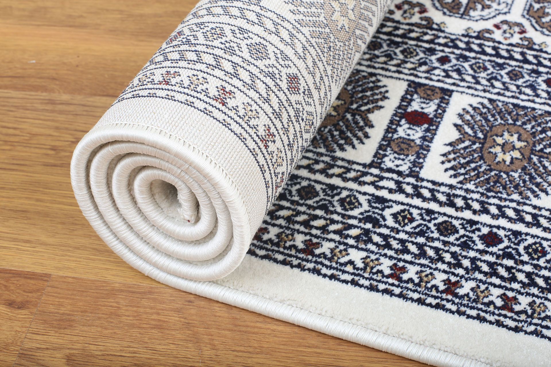 A white and blue rug is rolled up on a wooden floor.