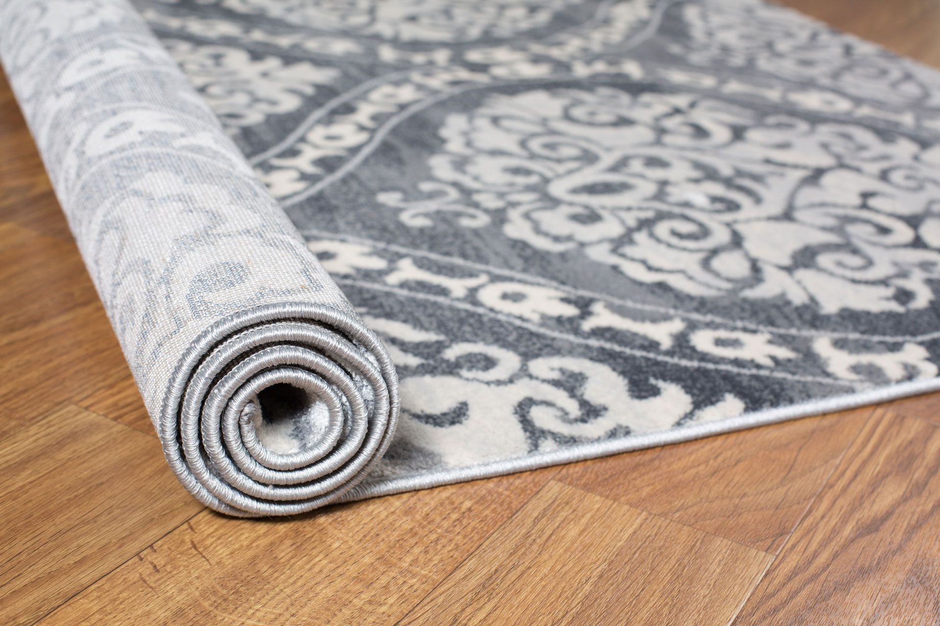 A gray and white rug is rolled up on a wooden floor.