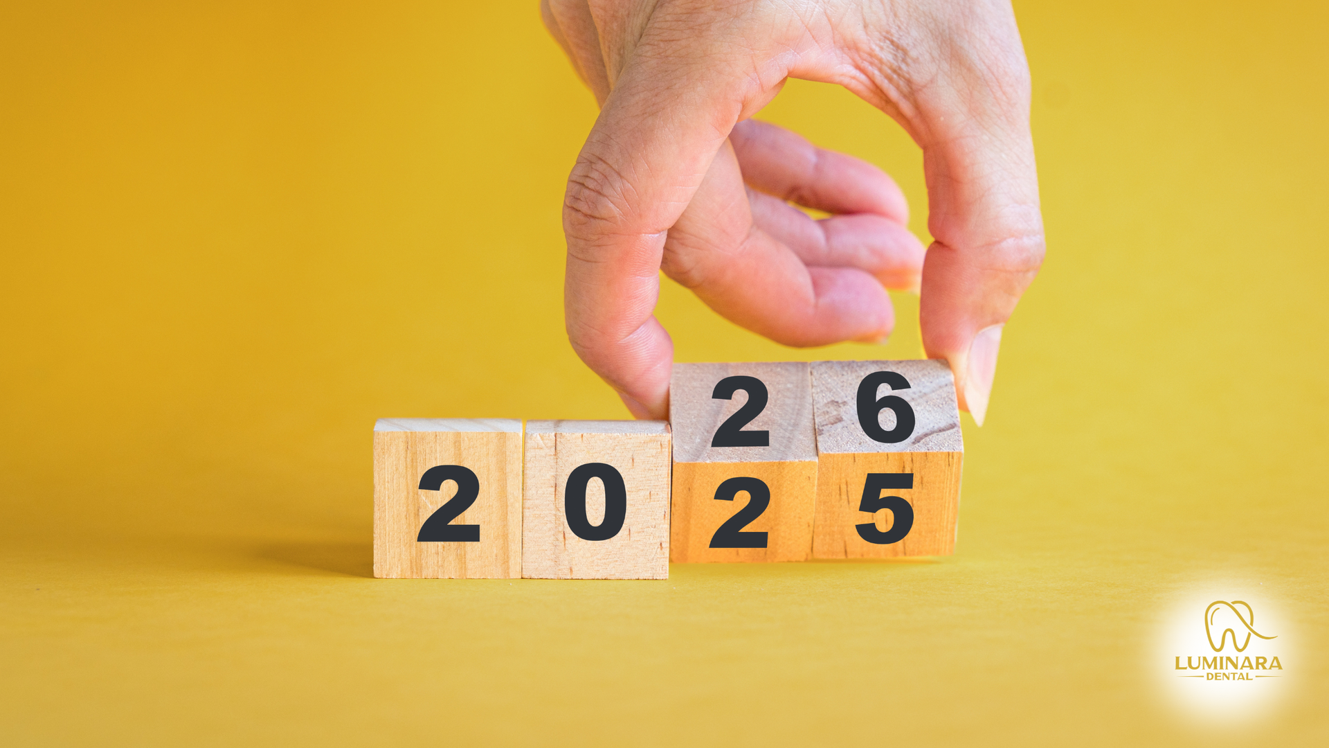 Hand flipping a wooden block from 2025 to 2026 on a yellow background.