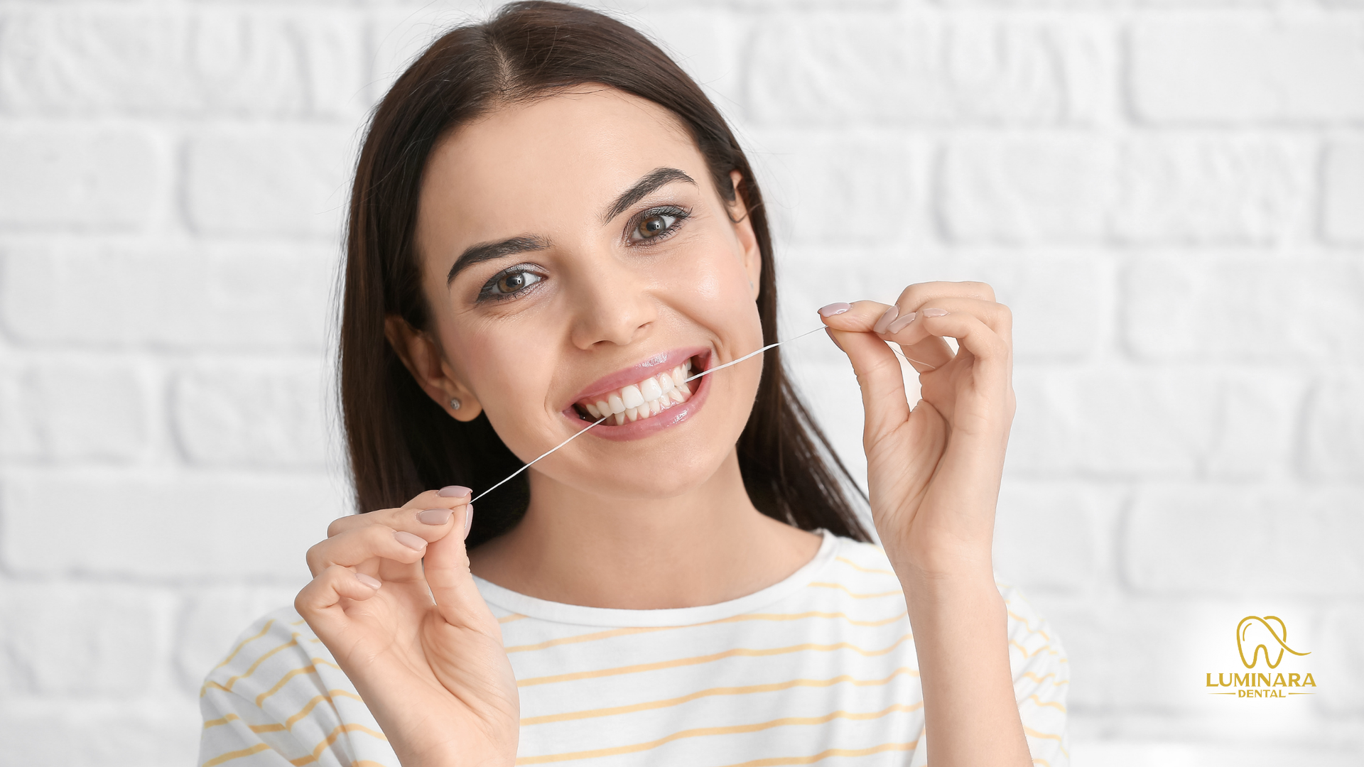 A woman is flossing her teeth in front of a white brick wall.